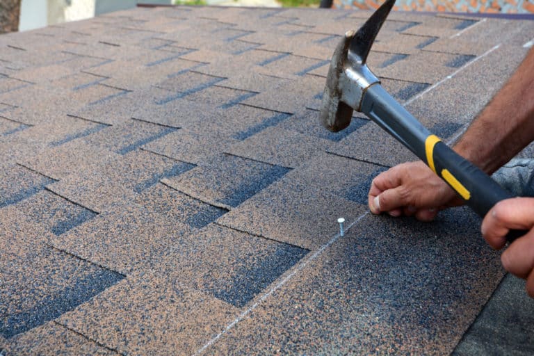 Worker hands installing bitumen roof shingles. Completing a full, not a partial roof replacement