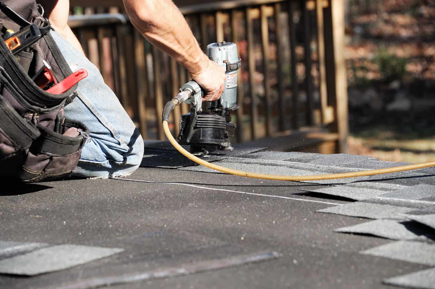 handyman using nail gun to install shingles on residential roof