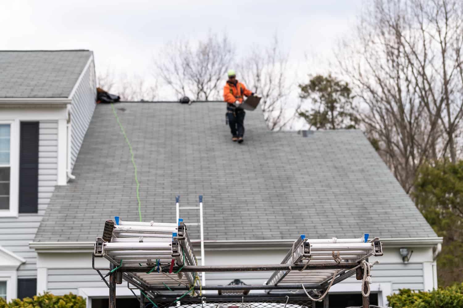 out of focus male worker walking down asphalt shingle roof with tools in hand