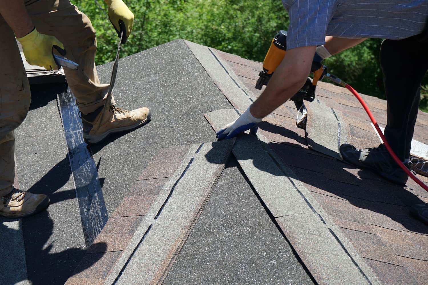 bottom half of two men installing Asphalt Shingles with nail gun on the roof of a new house.