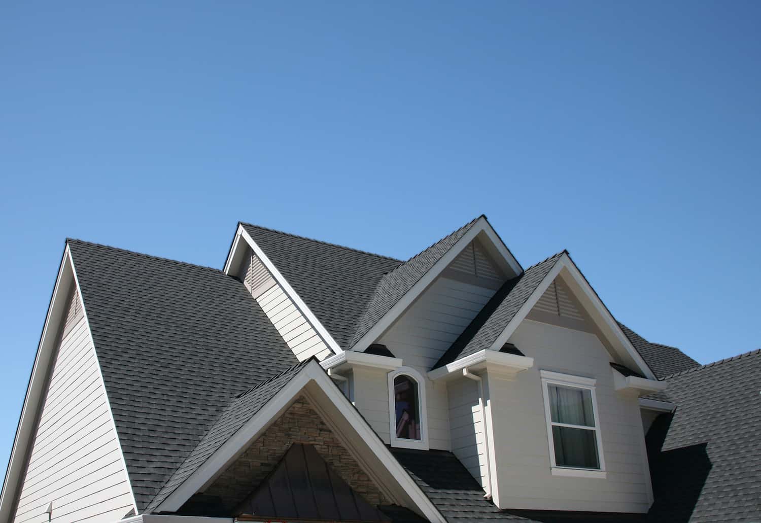 top half view of grey asphalt shingles on modern residential roof; blue sky in background