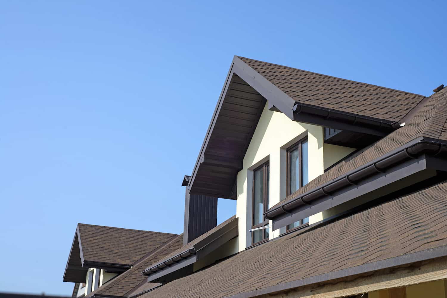 brown asphalt shingle roof with with windows and blue sky in background