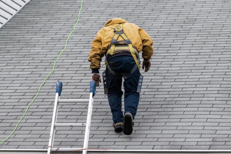 man in yellow uniform walking on roof shingles and ladder during repair
