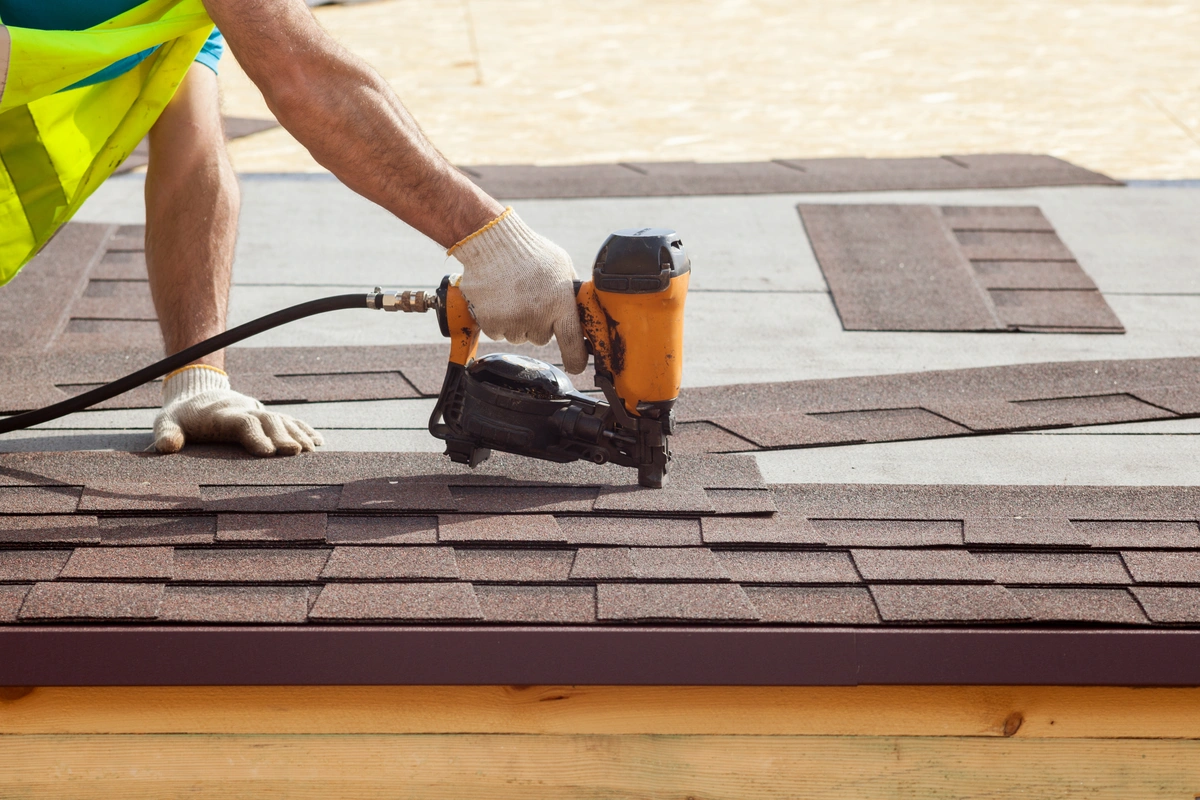 construction worker placing asphalt shingles on the roof