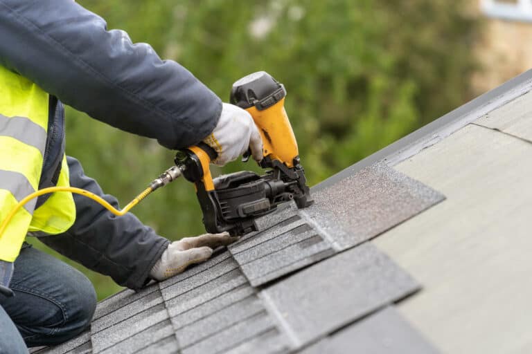 Unrecognizable roofer worker in uniform using nail gun to install shingles