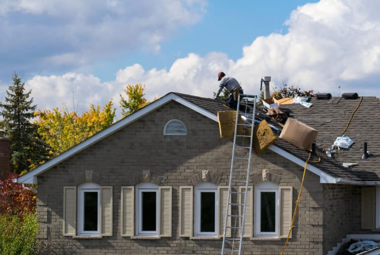 worker on the roof of a 2-story family house adding a new layer of asphalt shingles