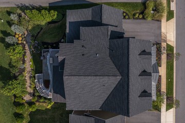 Aerial top down view of a complex hip and valley pitched roof with three dormers on a new construction American luxury single family house real estate